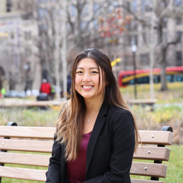MSU alumna Angela Yuan smiles while sitting on a wooden bench