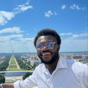 A person in a white shirt and glasses smiles with an aerial view of a city behind them